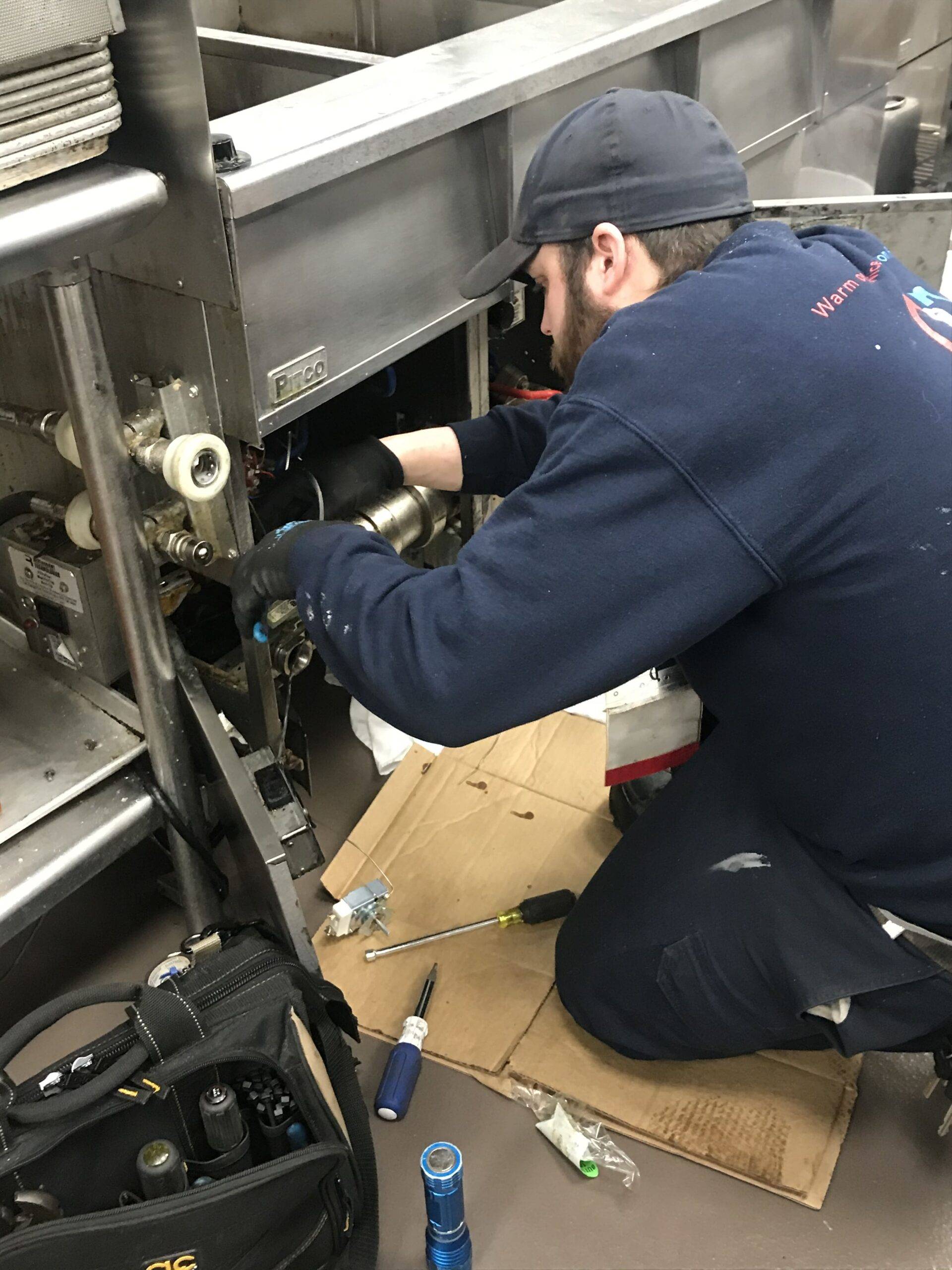 A technician wearing a navy blue sweatshirt is repairing an air conditioning unit